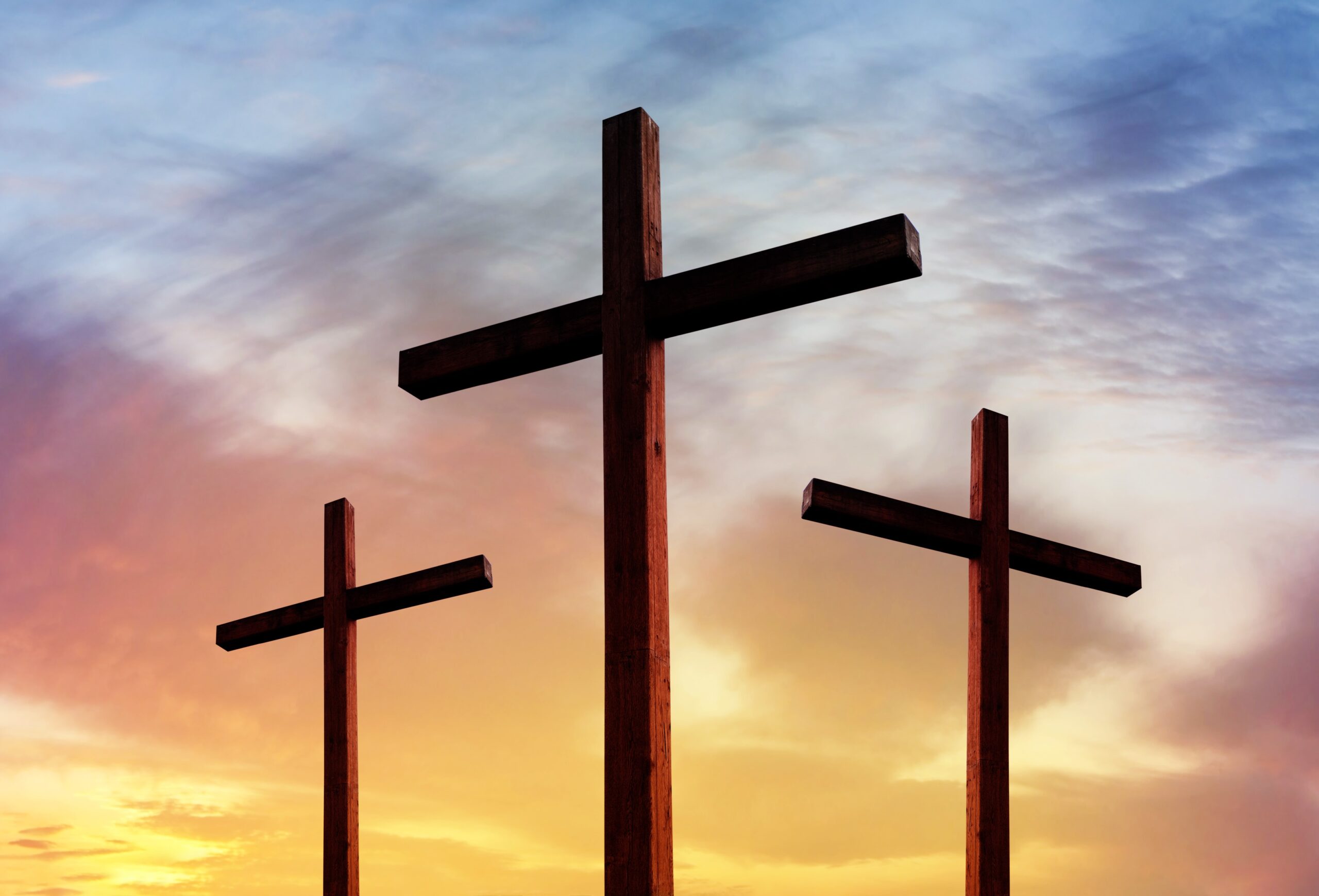 Three crosses with one in the foreground and a dramatic sunset in the background